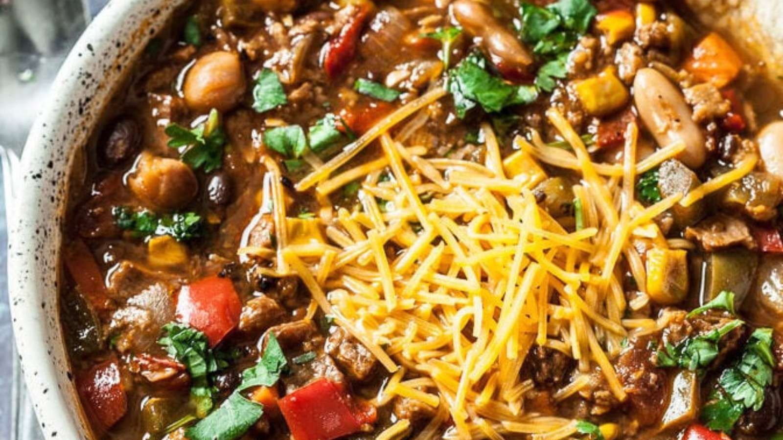A bowl of chili with cheese and vegetables.