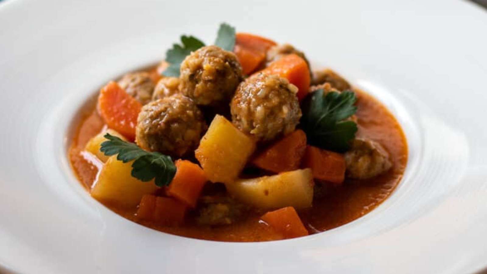 A bowl of stew with meatballs and carrots.