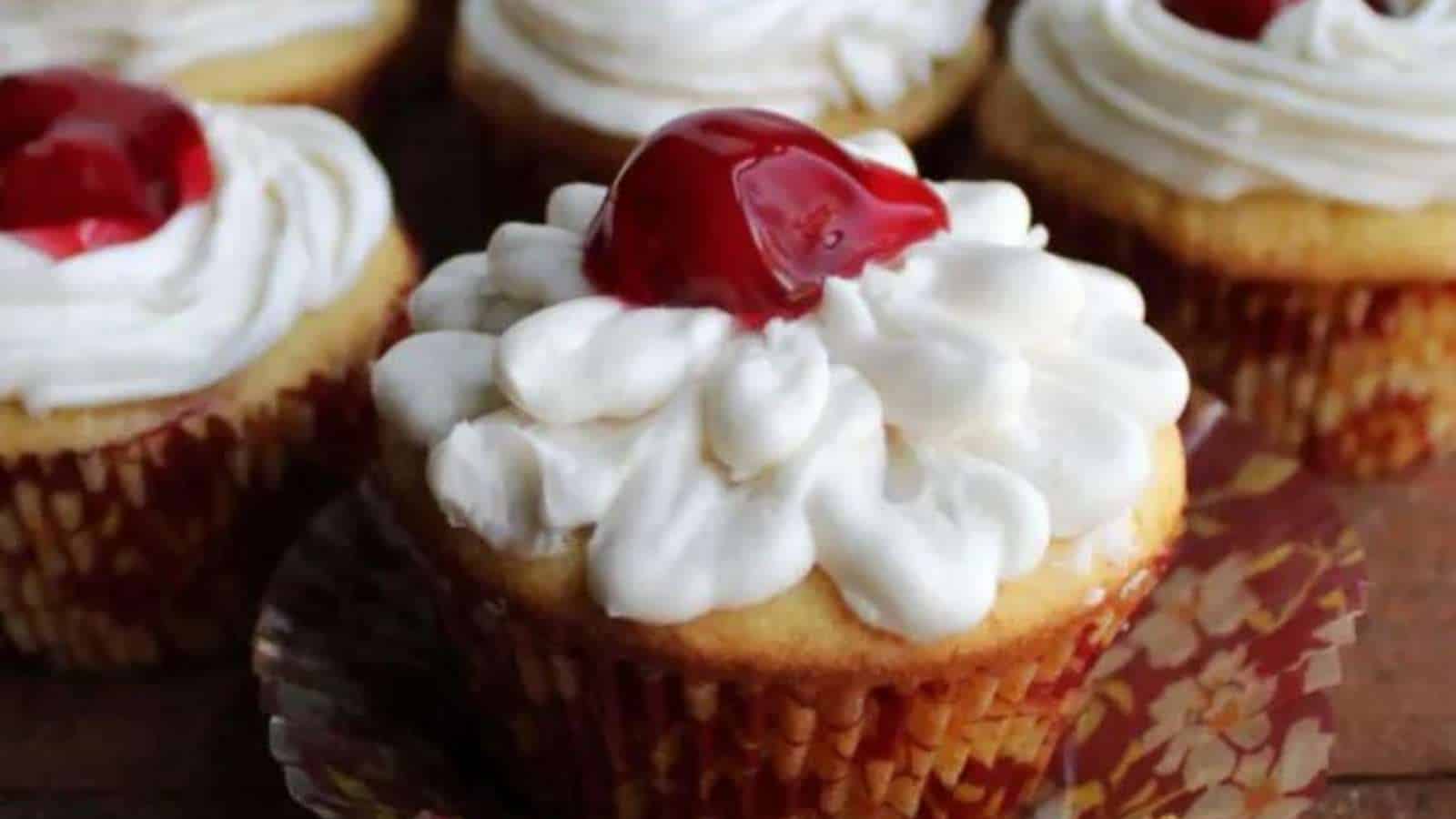 Cupcakes topped with whipped cream and cherries.