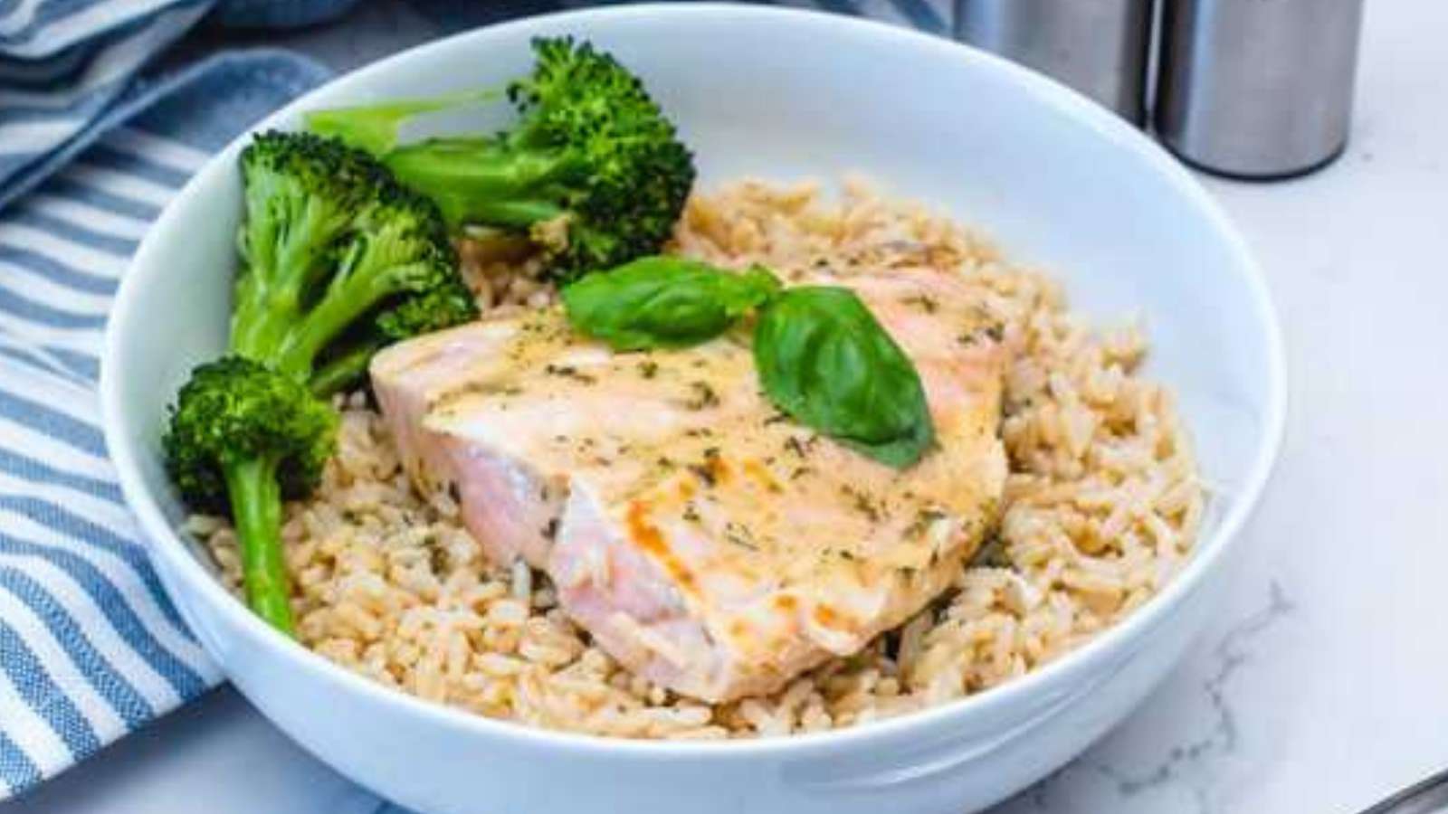 A white bowl filled with rice, salmon and broccoli.