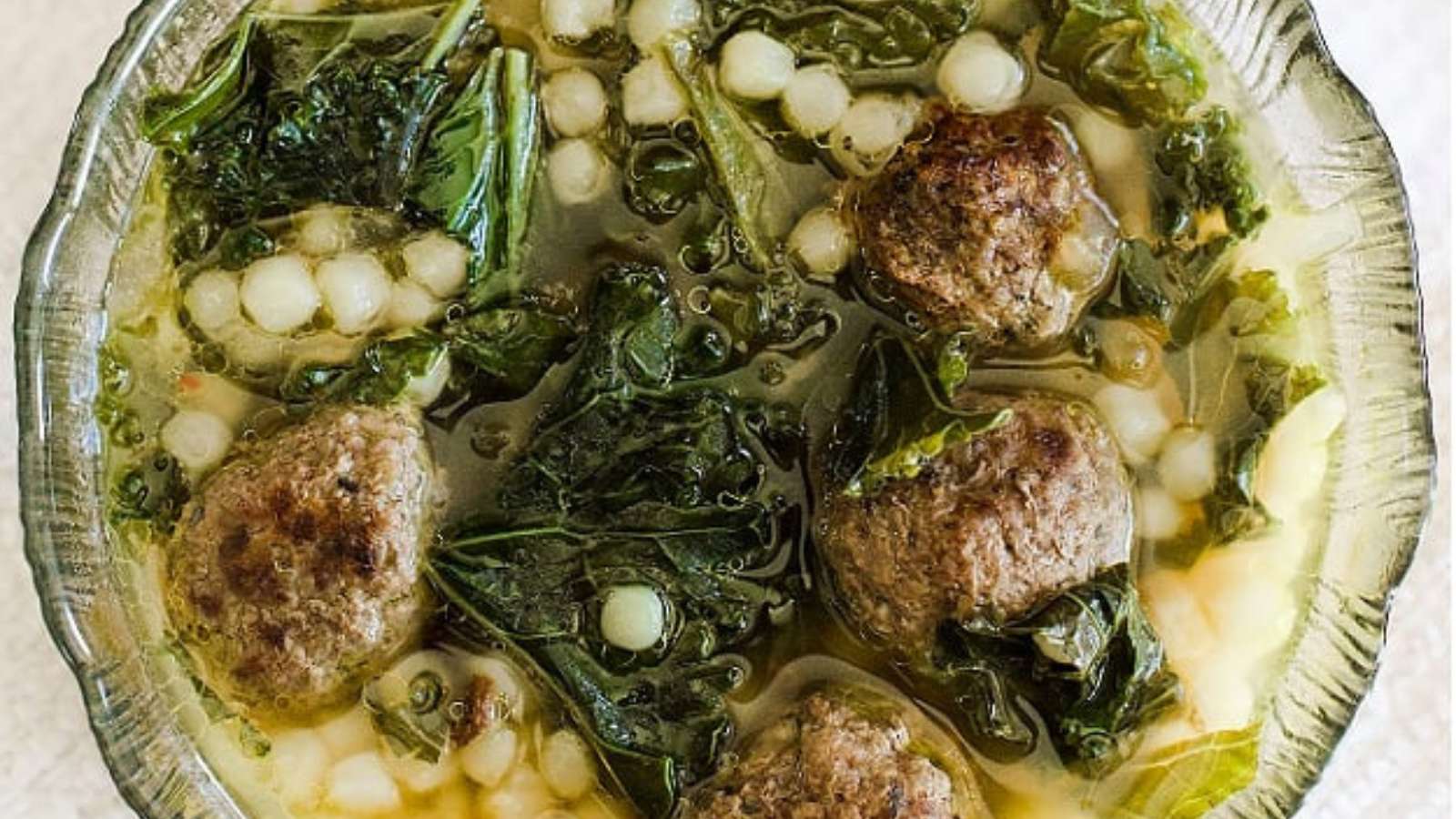 A bowl of soup with meatballs and greens.