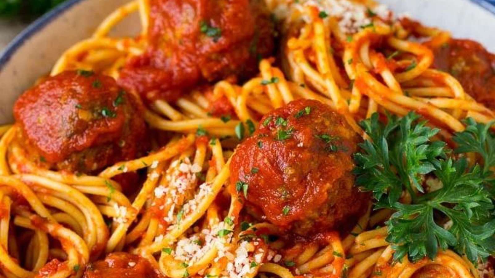 Spaghetti with meatballs and parsley in a blue bowl.