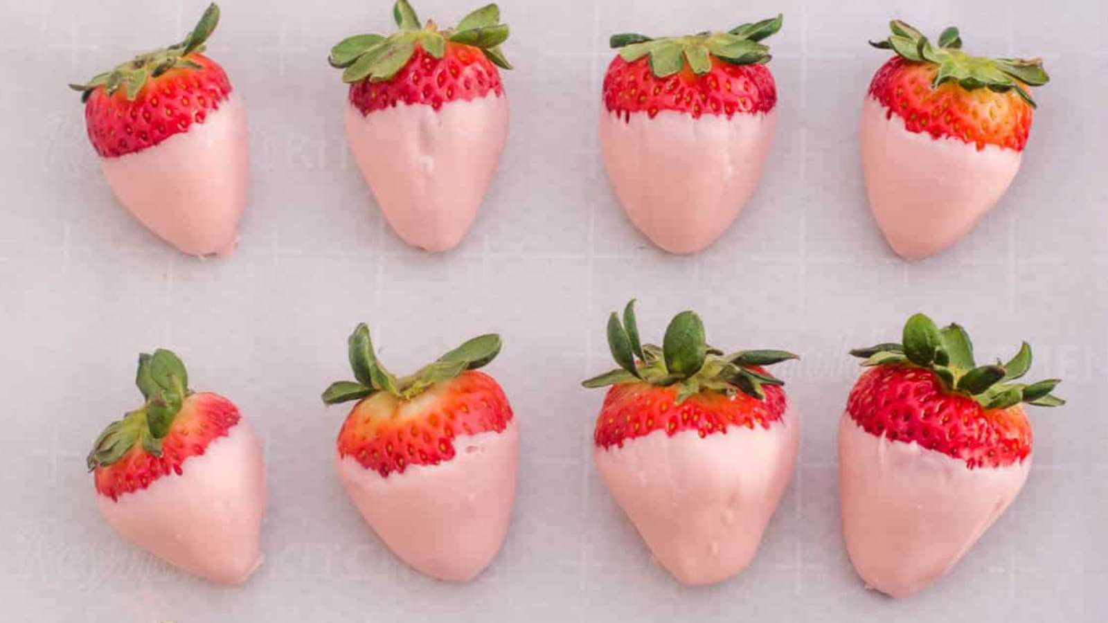 A group of pink strawberries are arranged on a white surface.