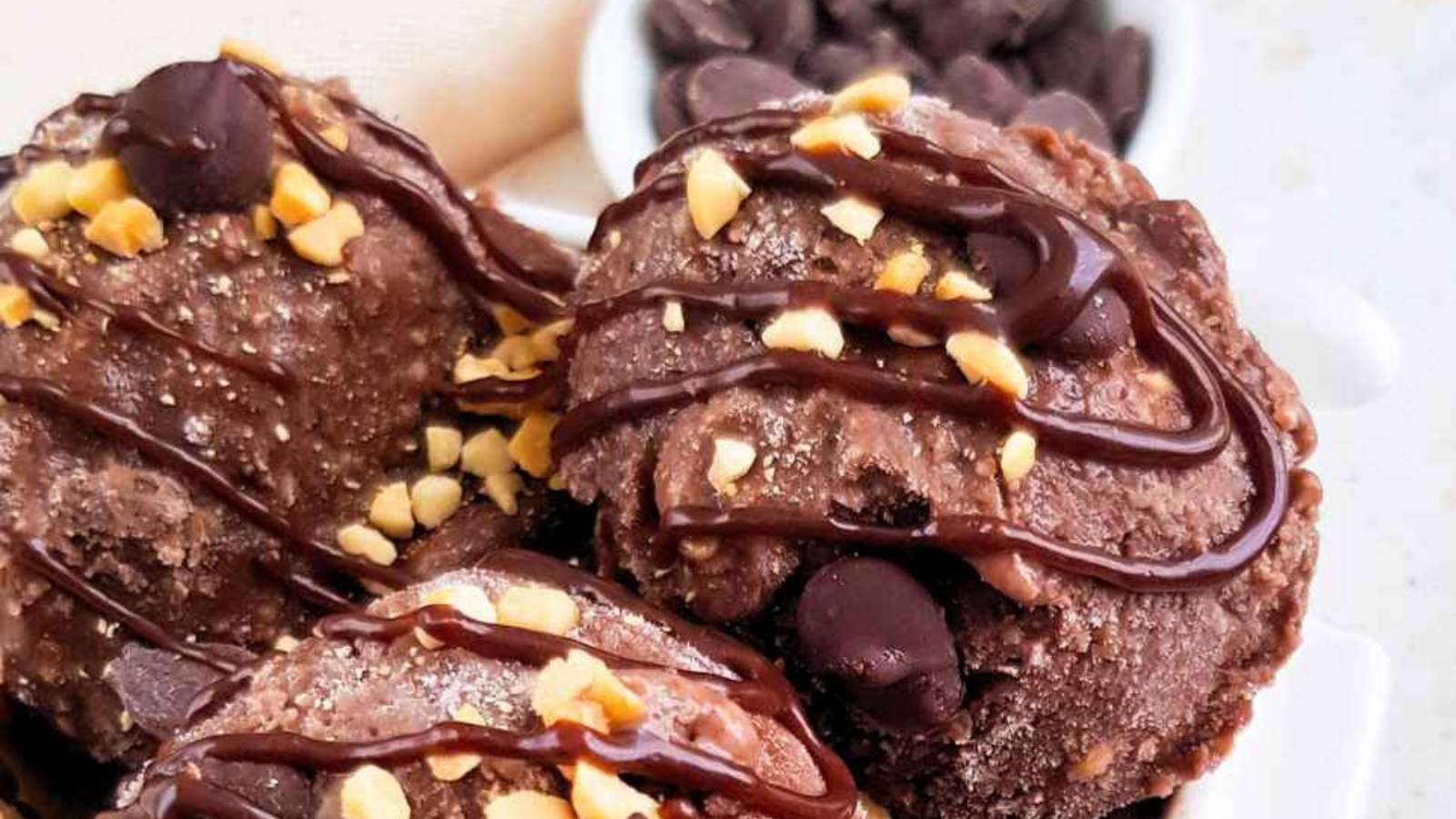 A bowl of chocolate ice cream topped with nuts and drizzled with chocolate.