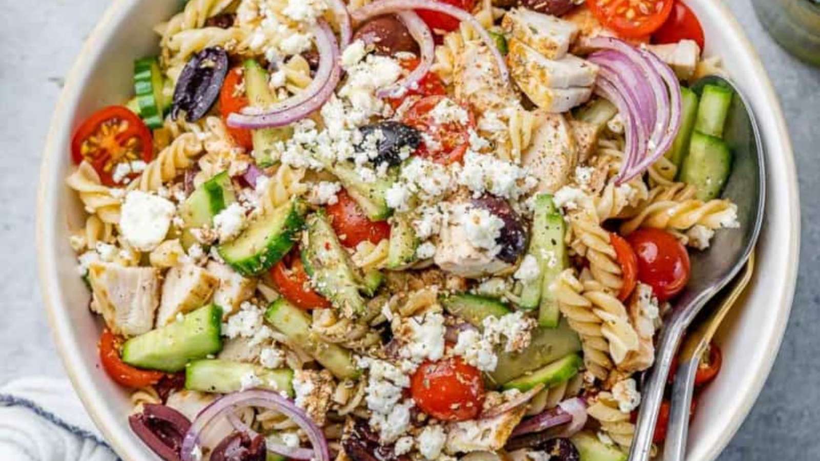 A bowl of greek pasta salad with chicken, tomatoes and cucumbers.