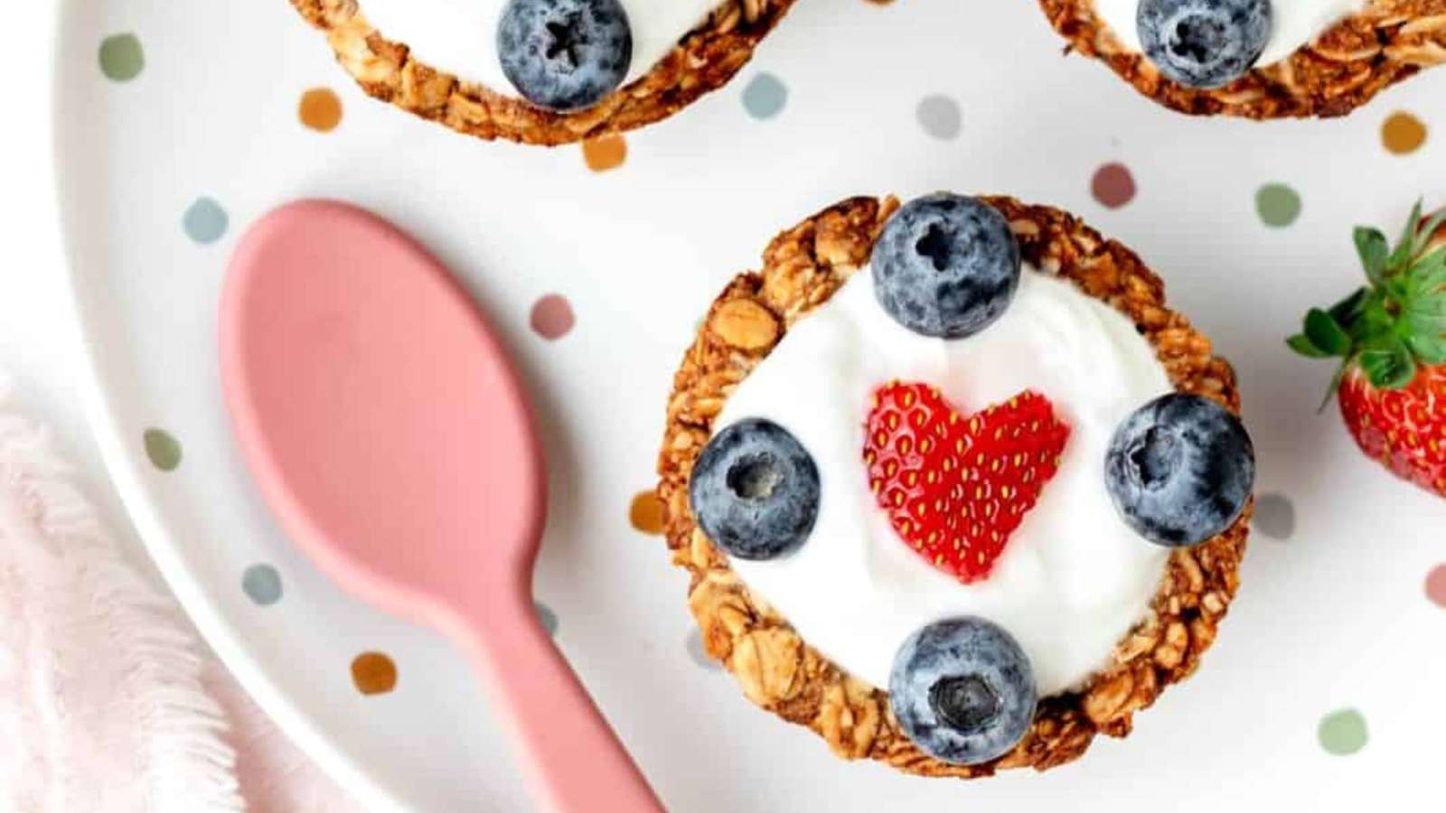 A heart shaped granola muffin with blueberries and strawberries on a plate.