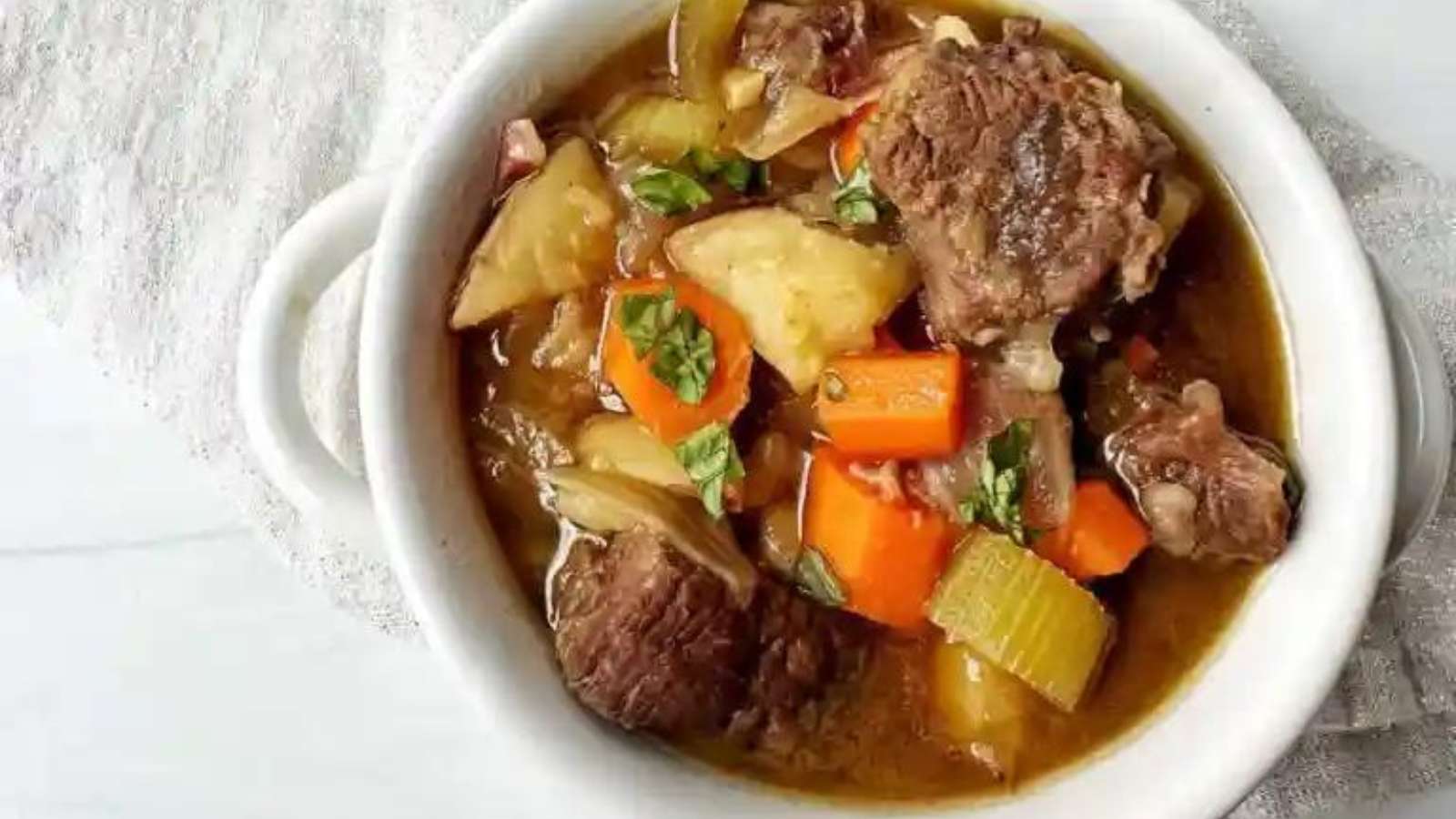 Beef stew in a white bowl with carrots and potatoes.