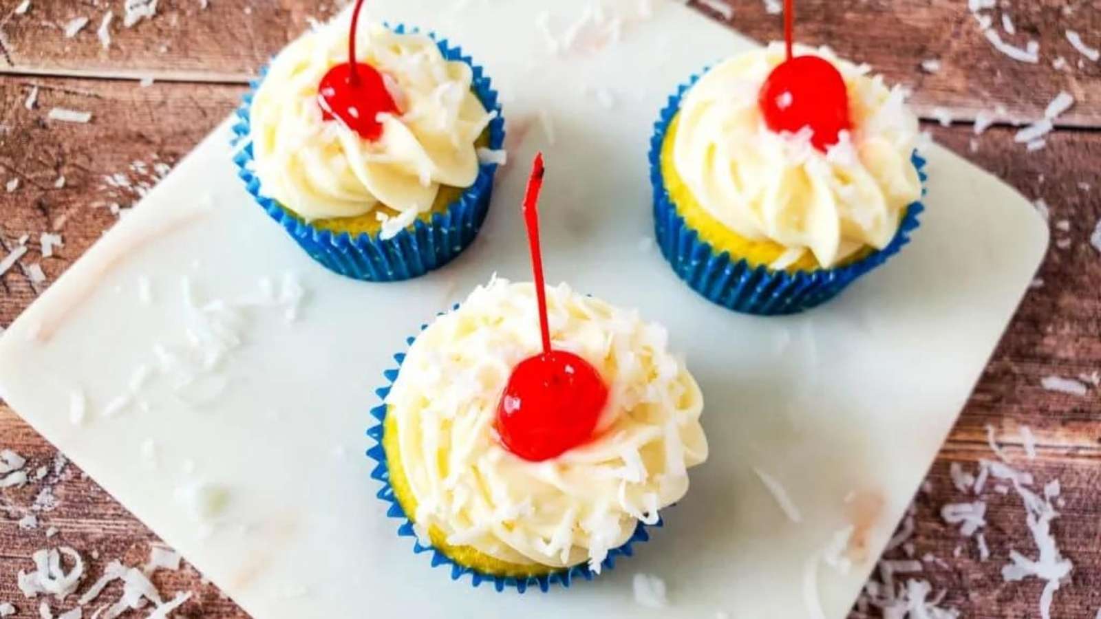 Three coconut cupcakes with a cherry on top.