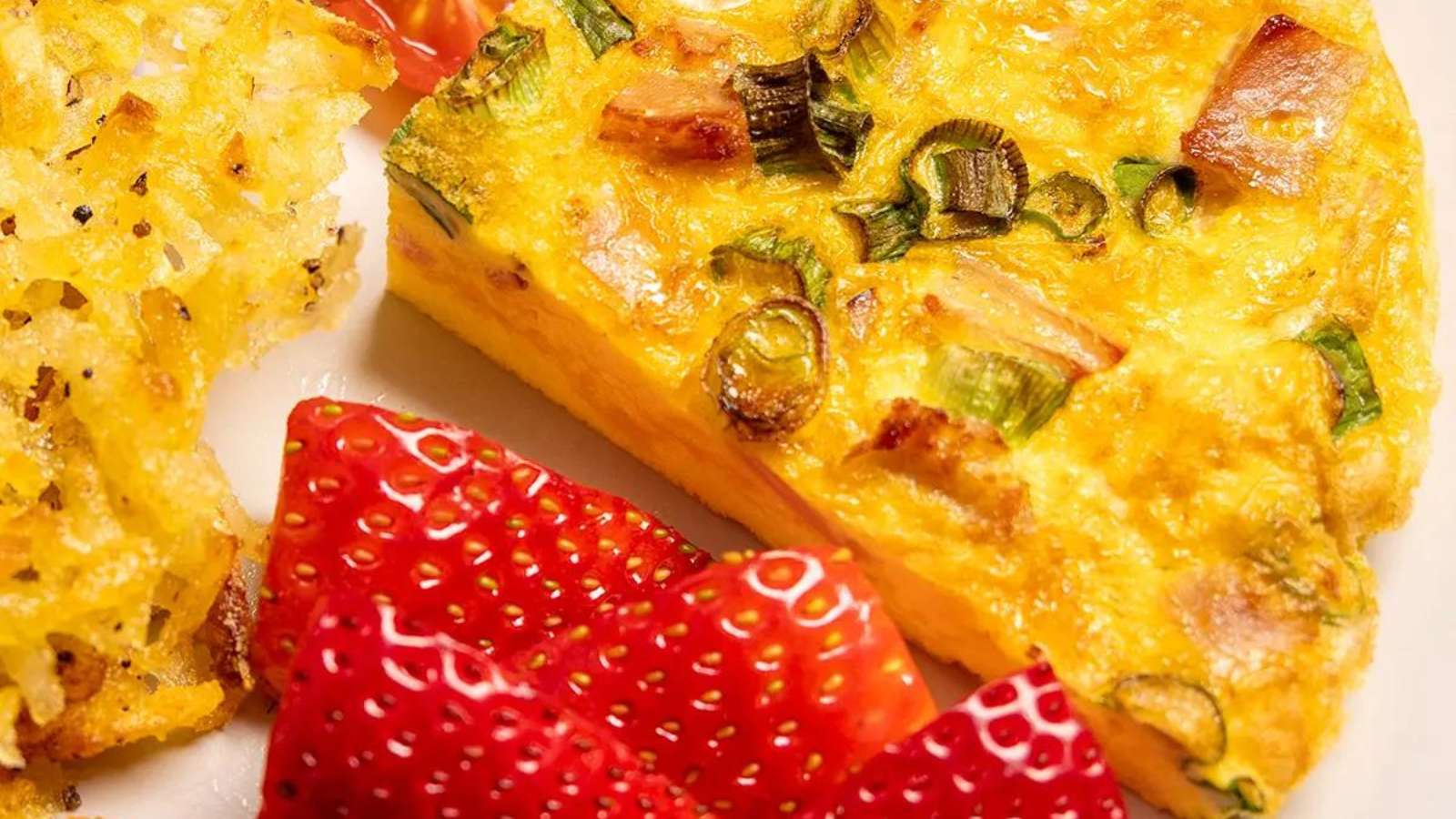 A slice of quiche and strawberries on a plate.