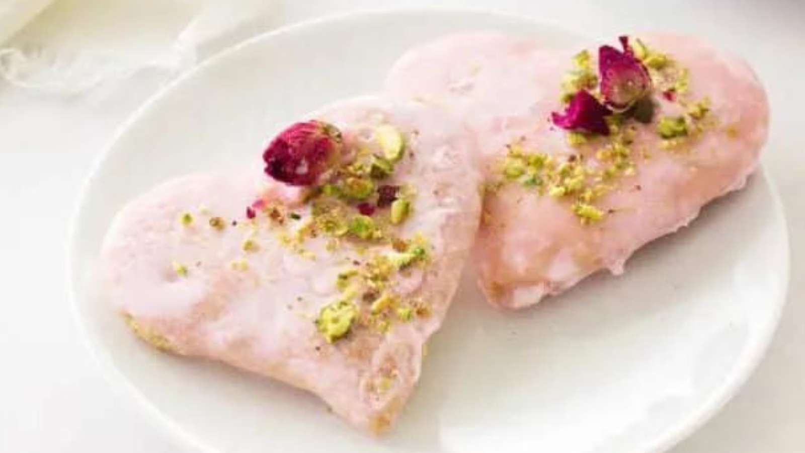 Two pink heart shaped cookies with pistachios on a plate.