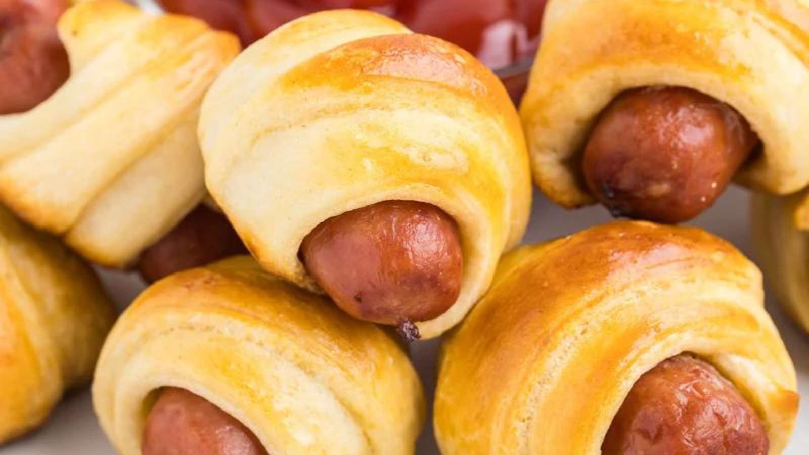 Hot dogs wrapped in pastry with ketchup on a plate.
