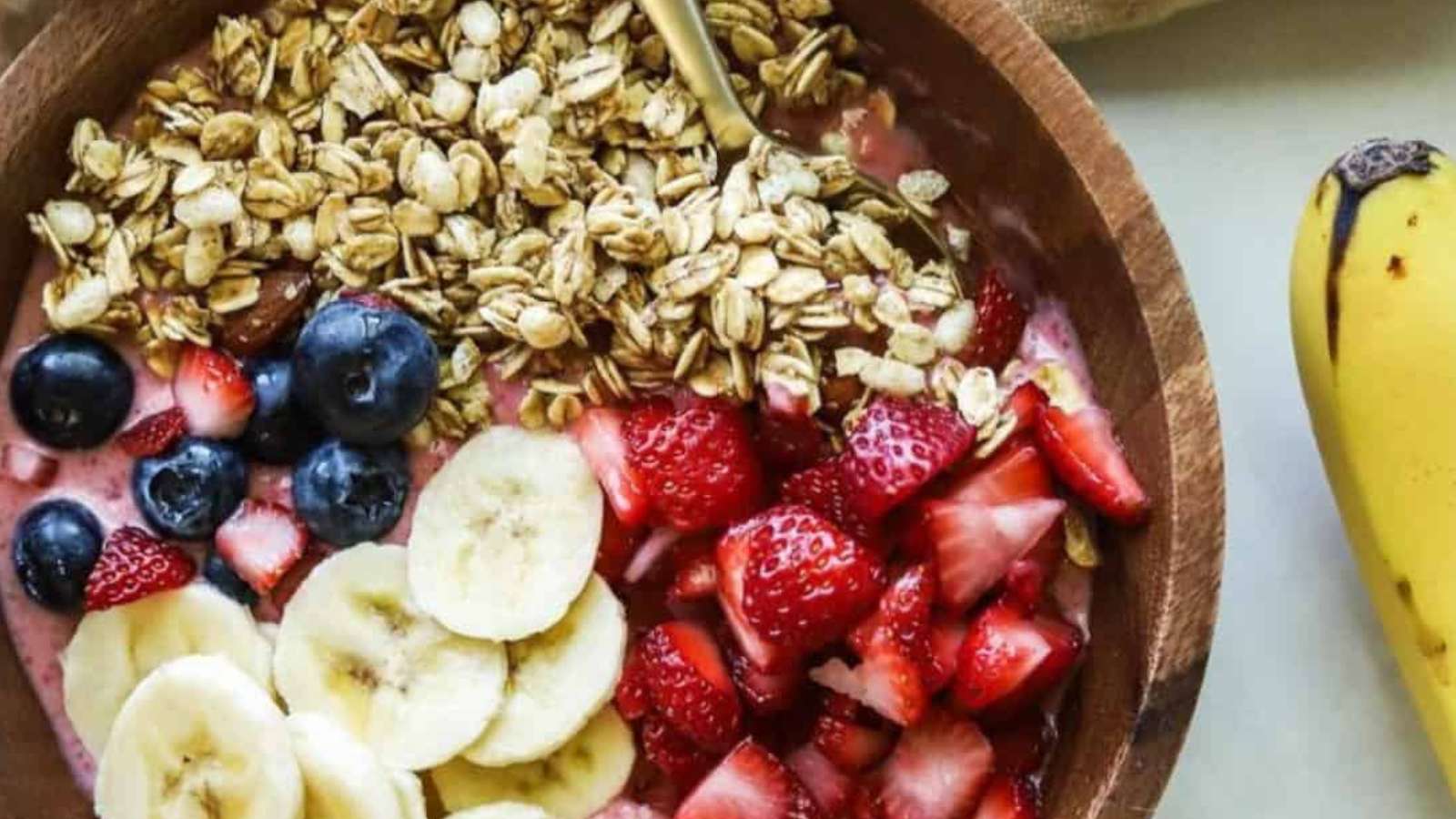 A bowl of fruit and granola with bananas and berries.