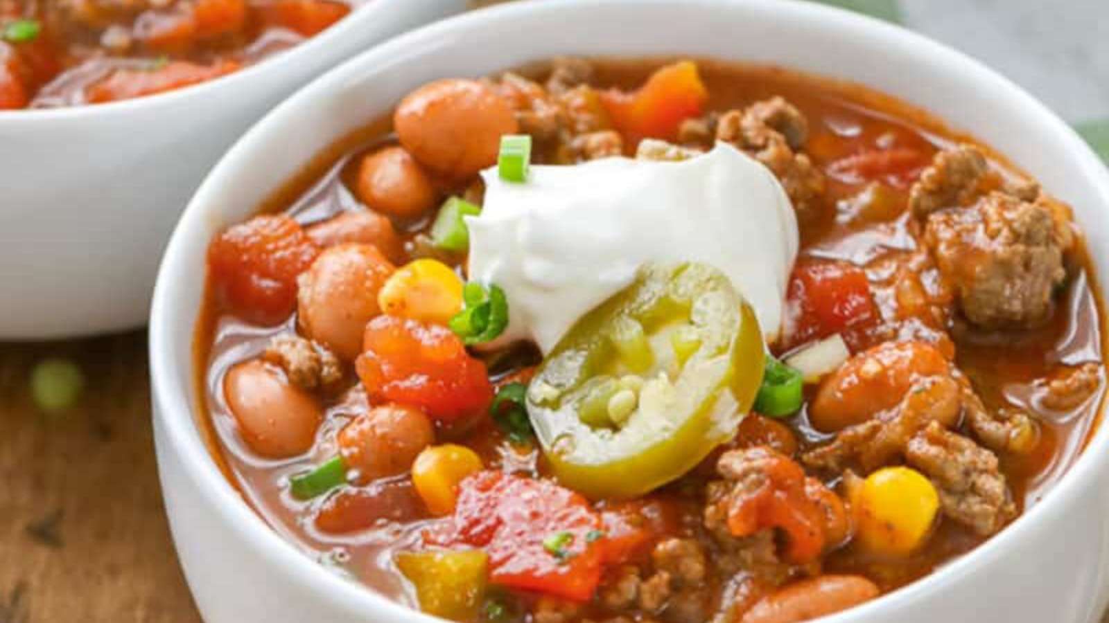Two bowls of chili with beans, corn and sour cream.