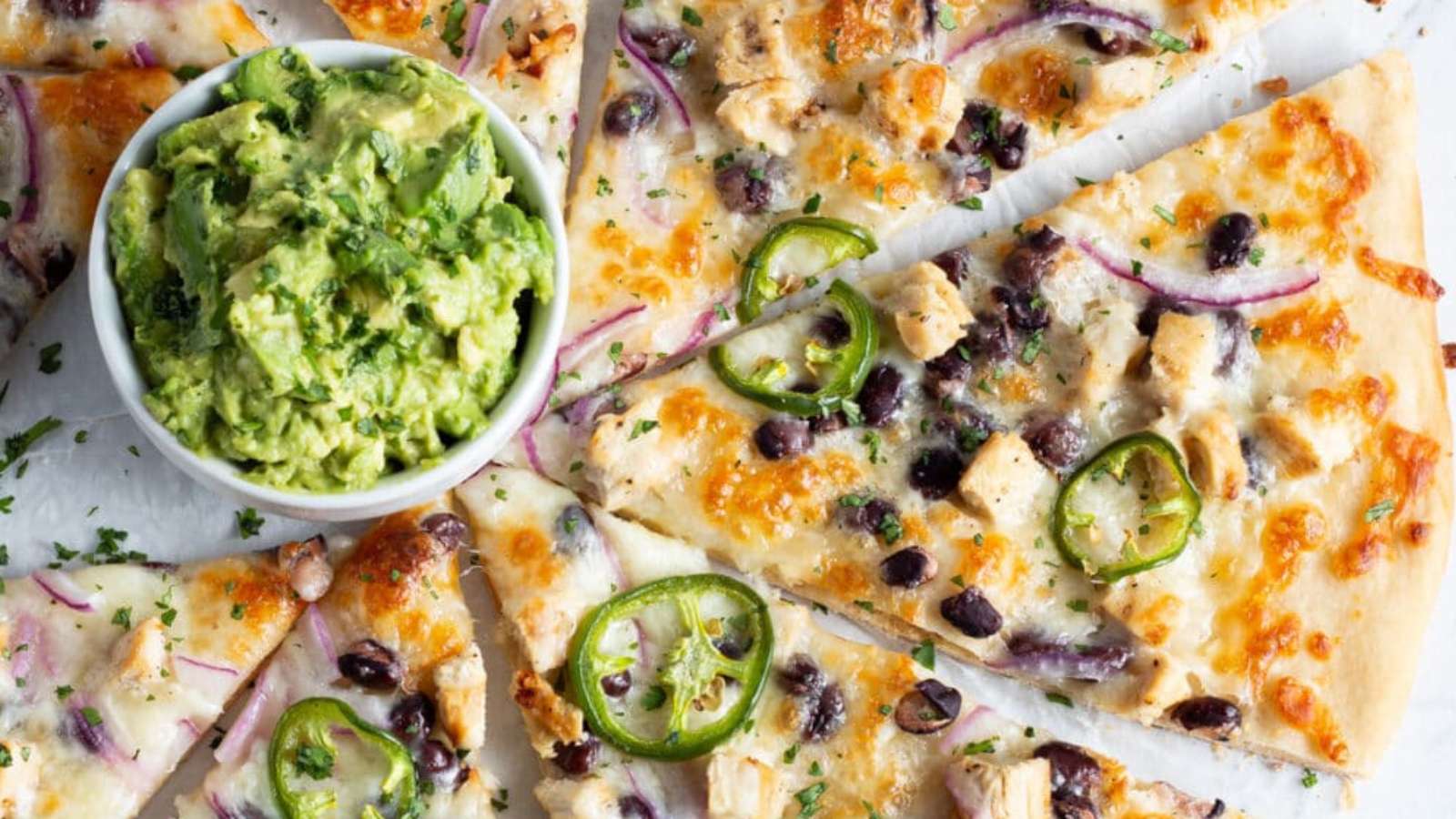 A slice of pizza with guacamole and black olives.