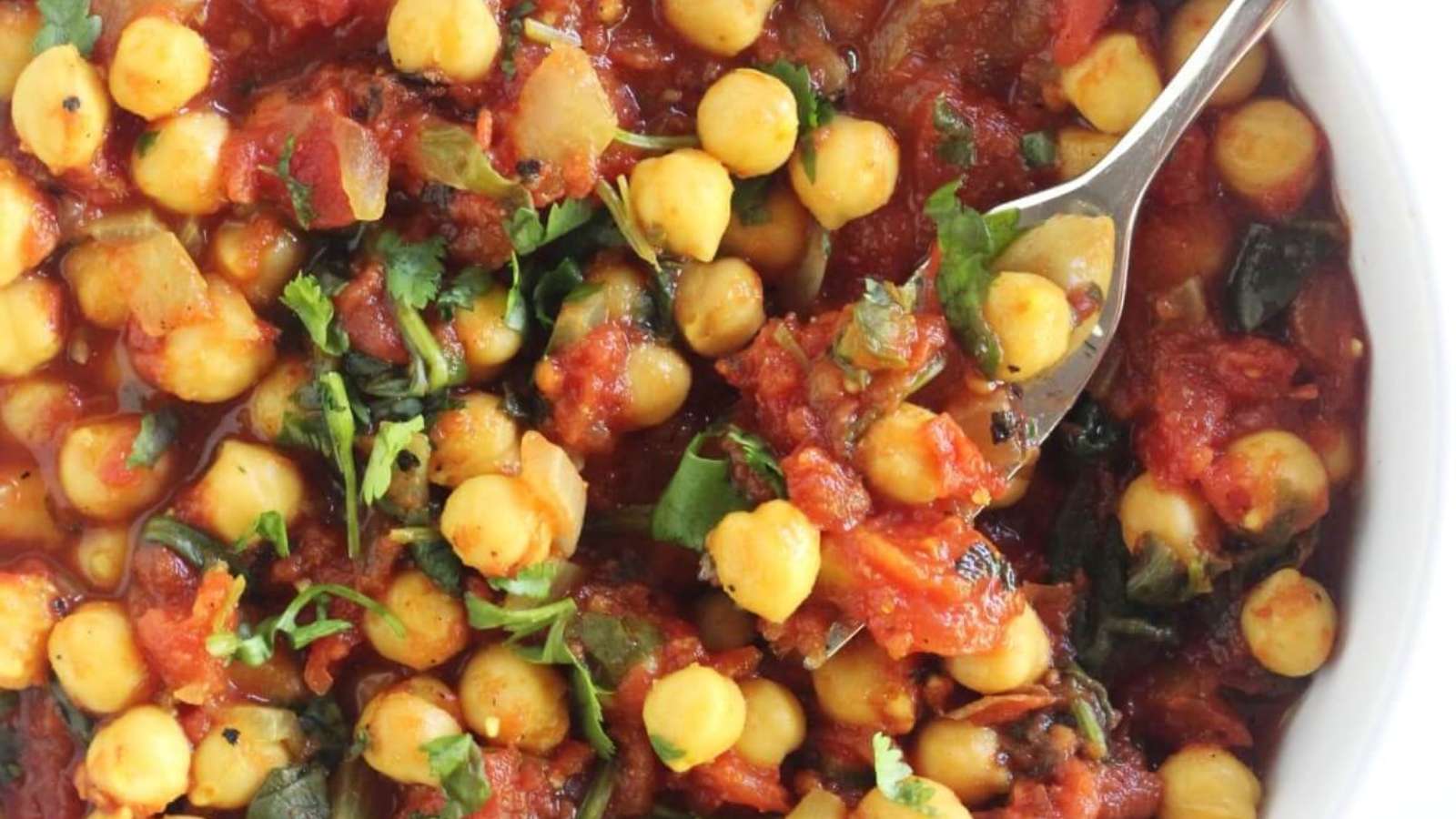 A bowl of chickpeas and tomatoes with a spoon.