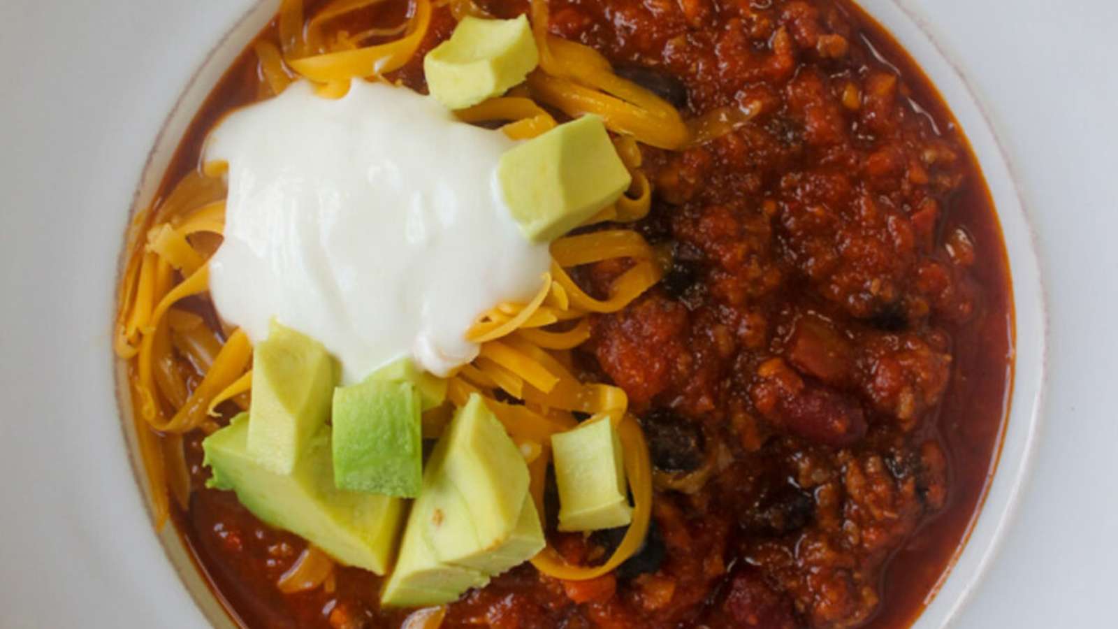 A bowl of chili with avocado and sour cream.