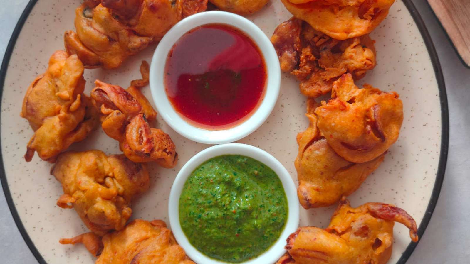 A plate with fried onion pakora and dipping sauce.