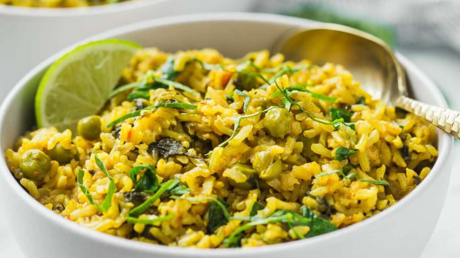 A bowl of yellow rice with peas and spinach.