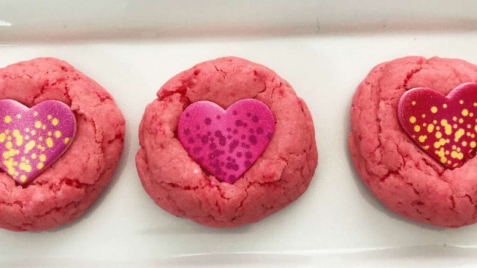 Three pink heart shaped cookies on a plate.