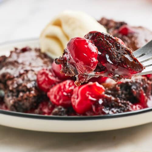 A fork is being used to eat a brownie with cherries and ice cream.