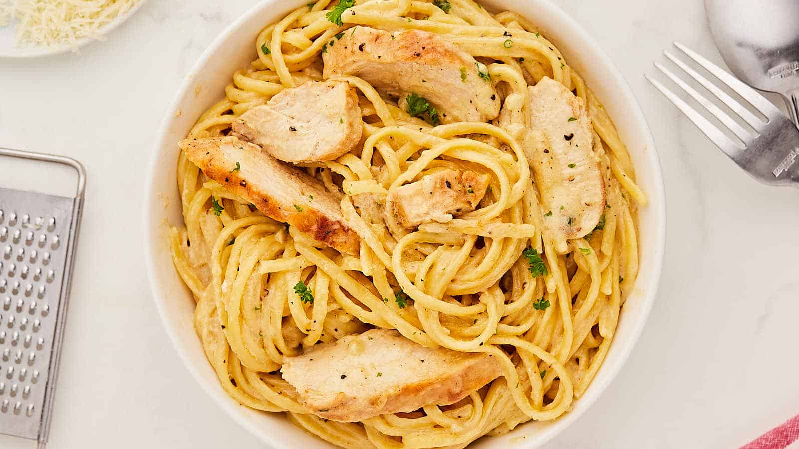A white bowl of pasta with chicken and parmesan.