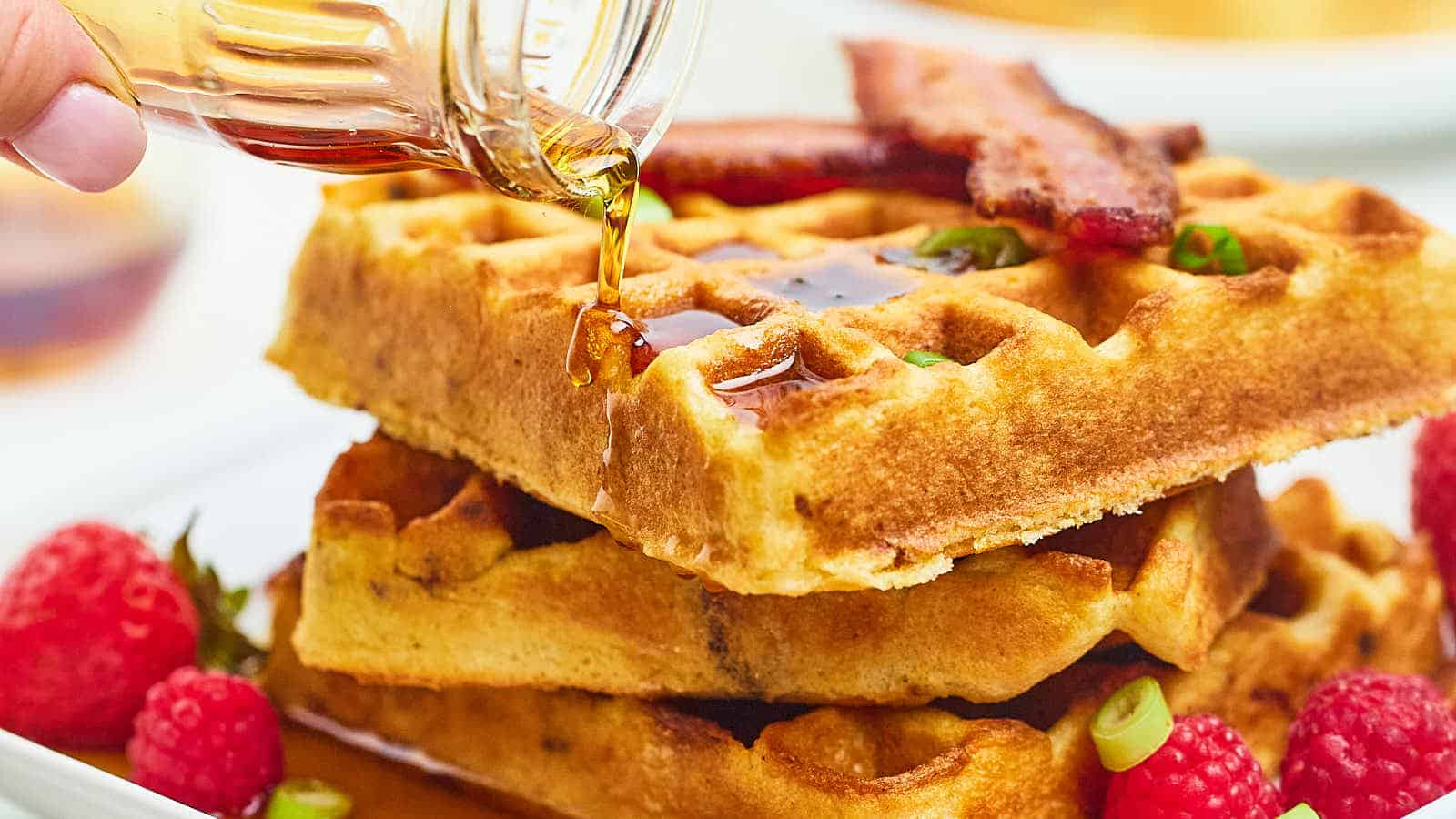 A person is pouring syrup on a stack of waffles.