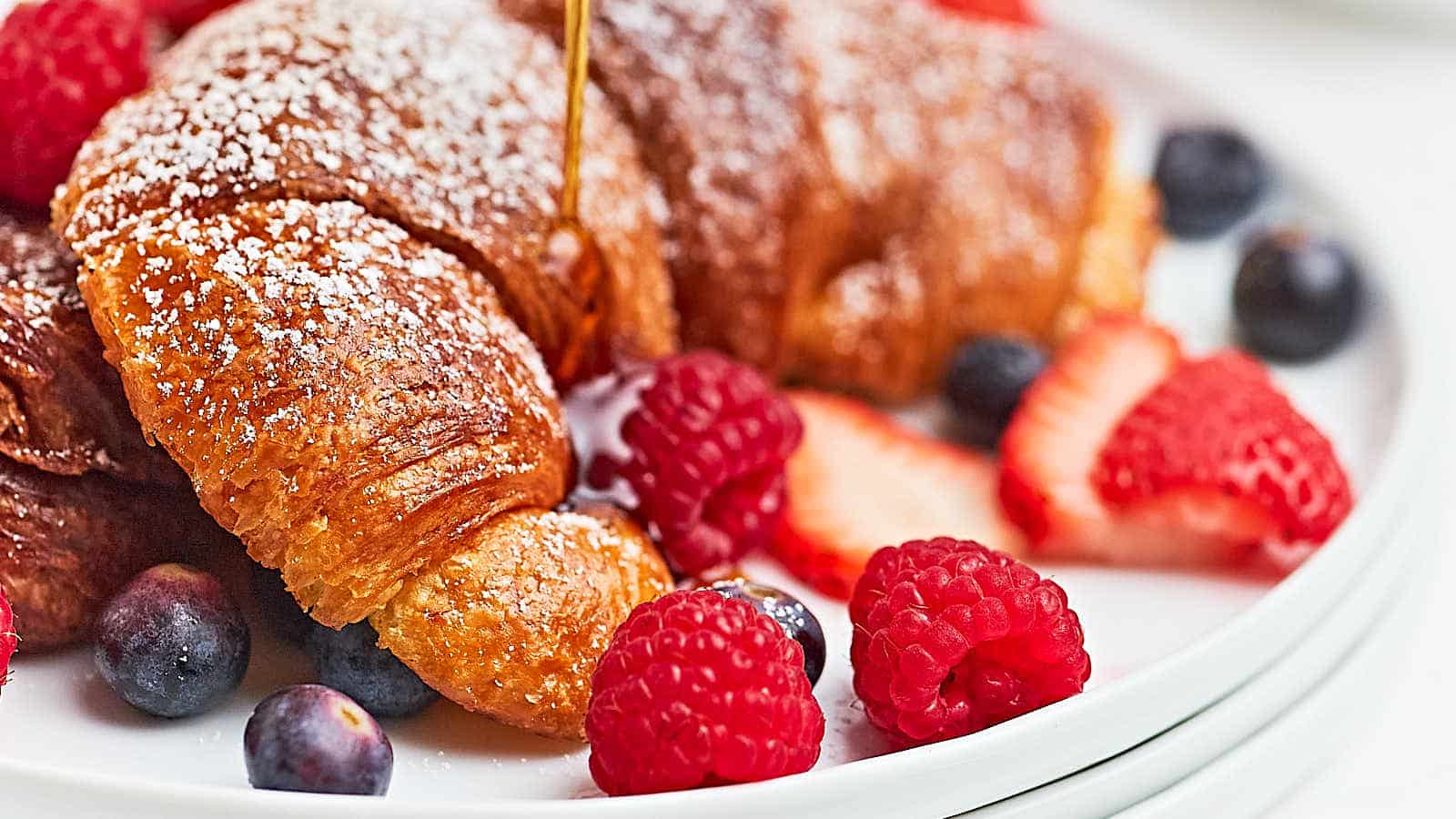 A plate of croissants with berries and syrup.