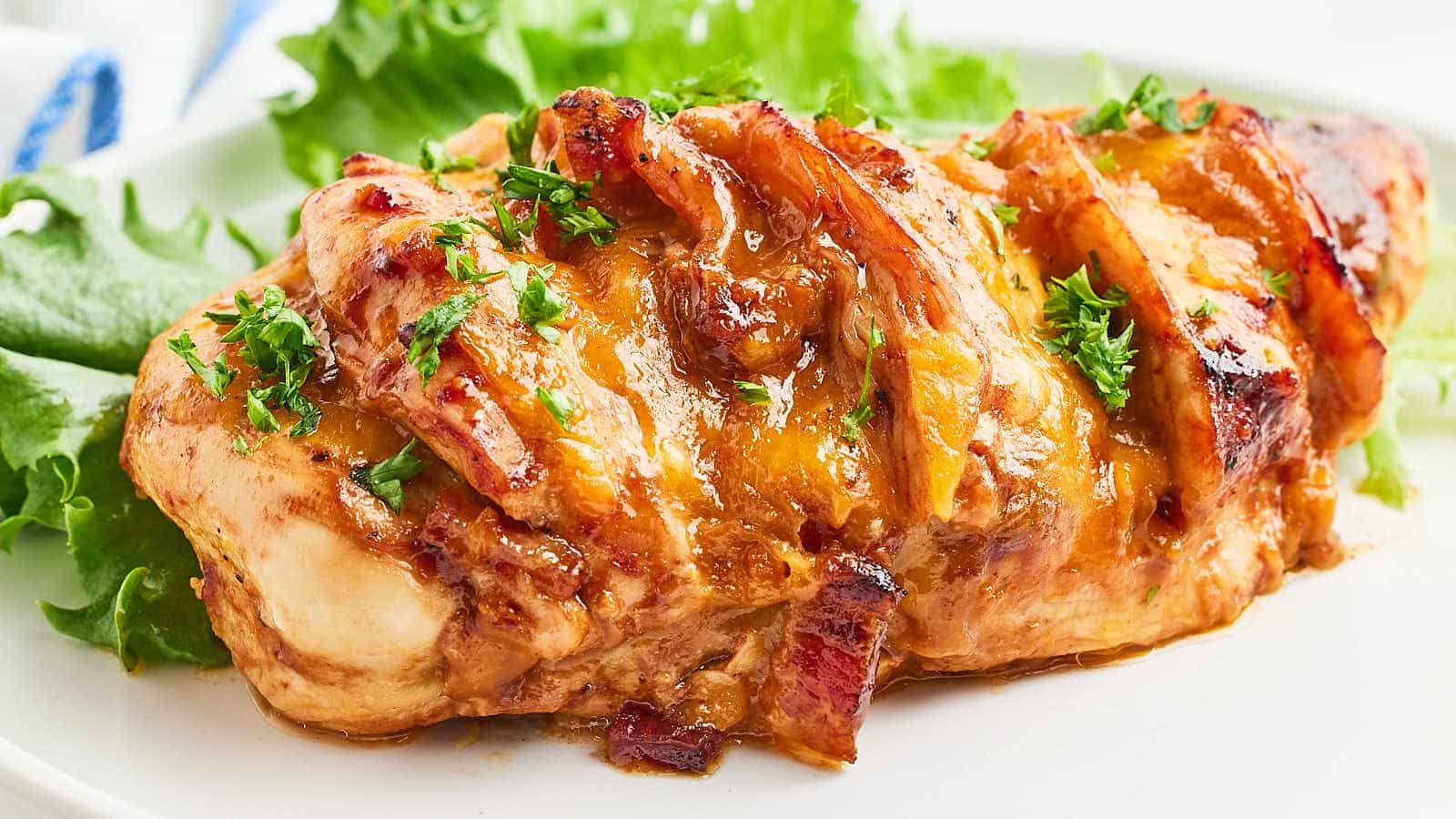 A chicken breast topped with bacon and lettuce on a white plate.