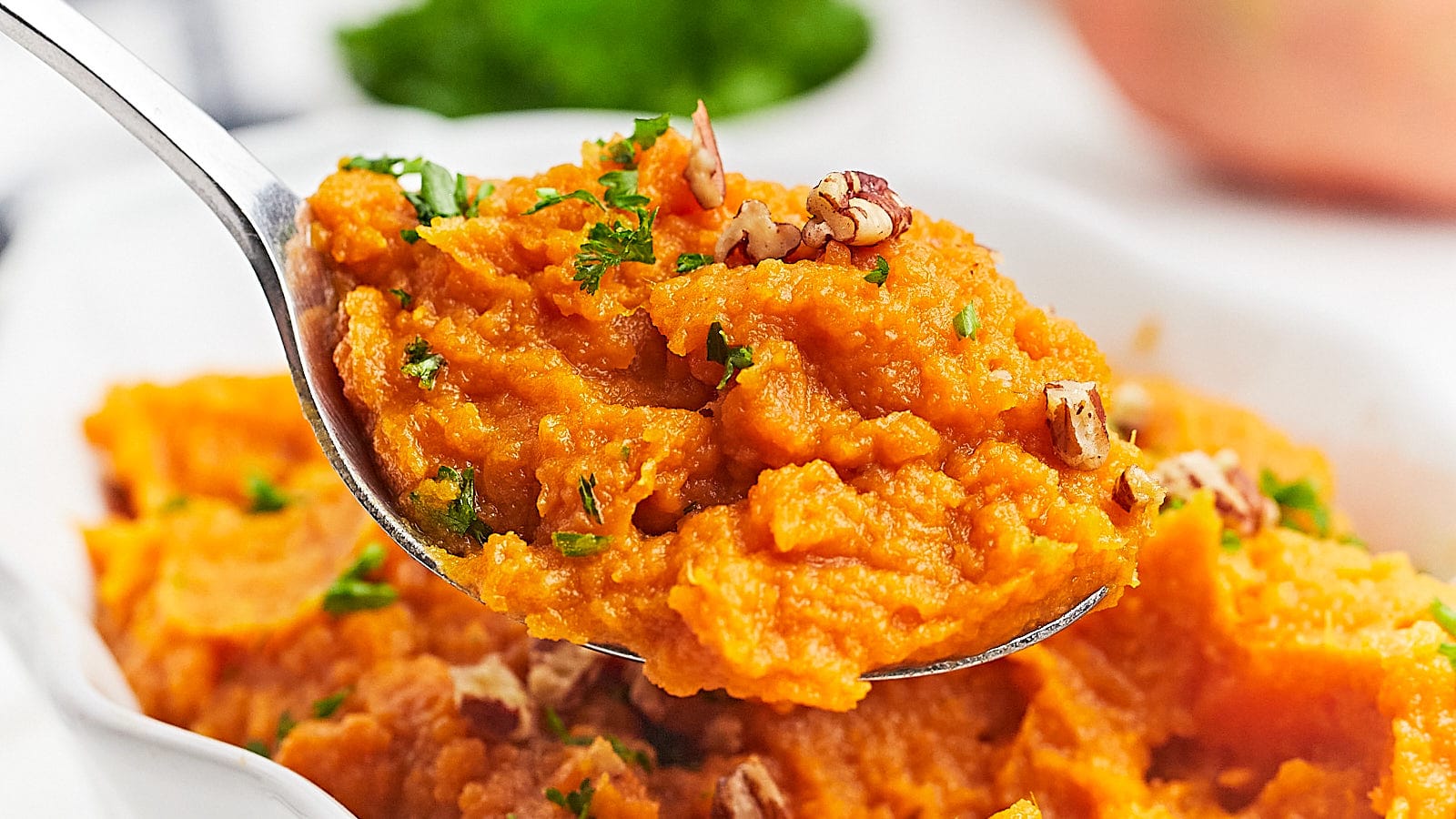 A spoon full of mashed sweet potatoes with pecans and parsley.