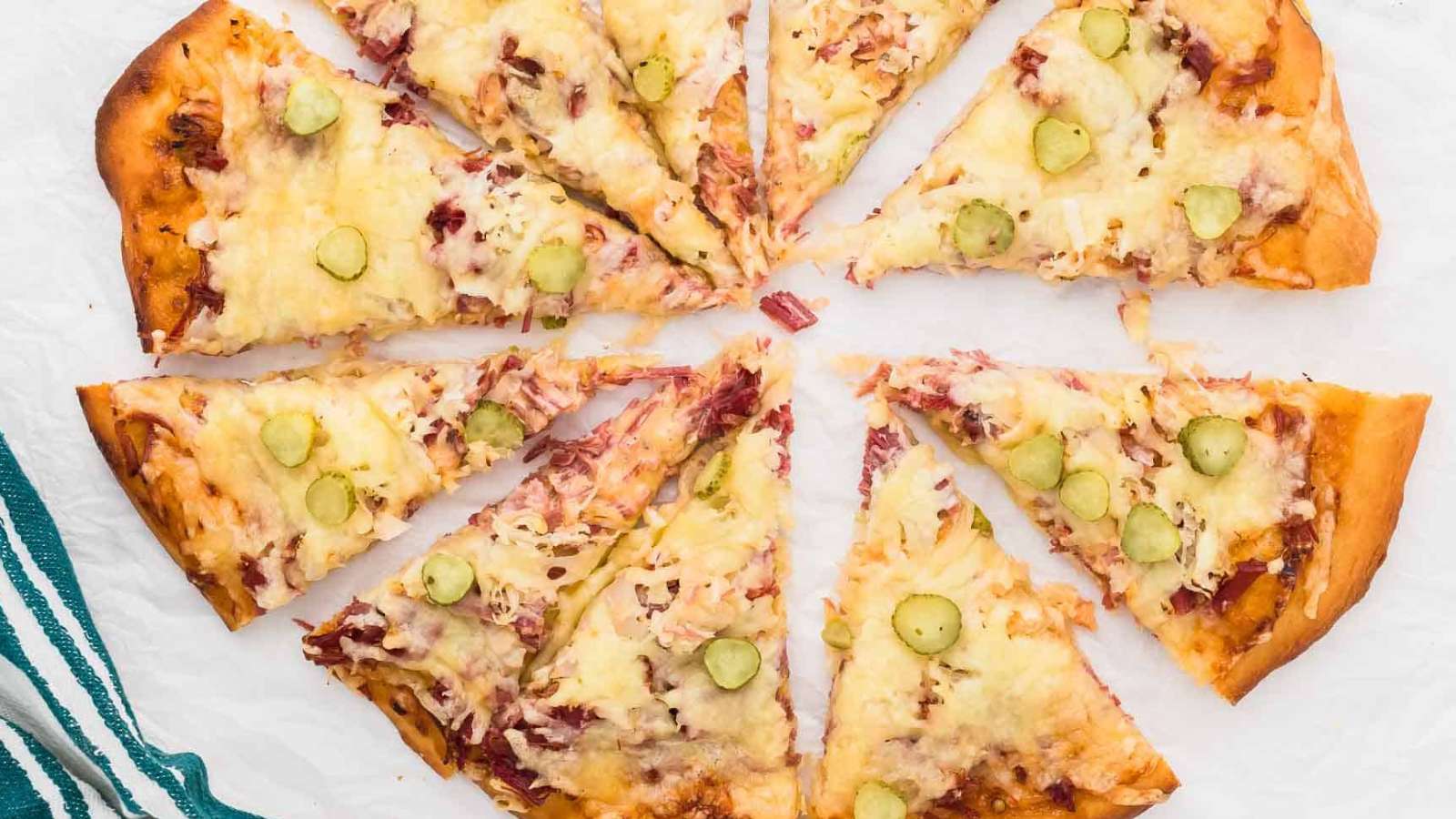 A slice of Reuben pizza with ham and pickles.