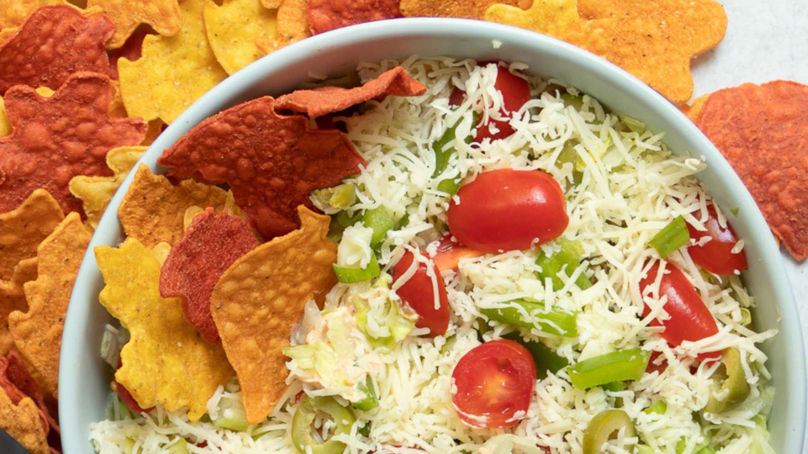 A bowl of cheese and vegetable dip with tortilla chips.