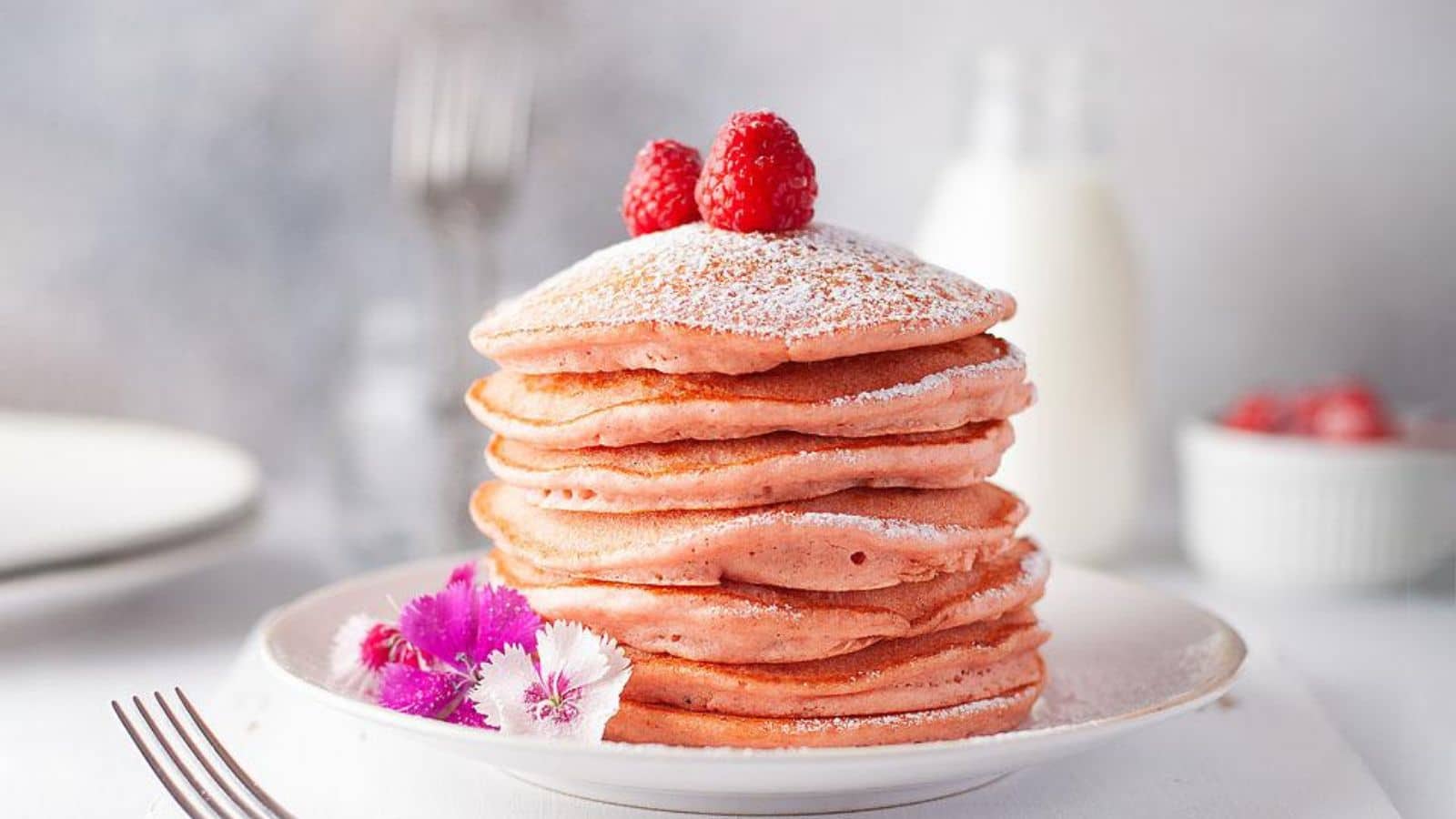 A stack of pancakes with raspberries and powdered sugar.