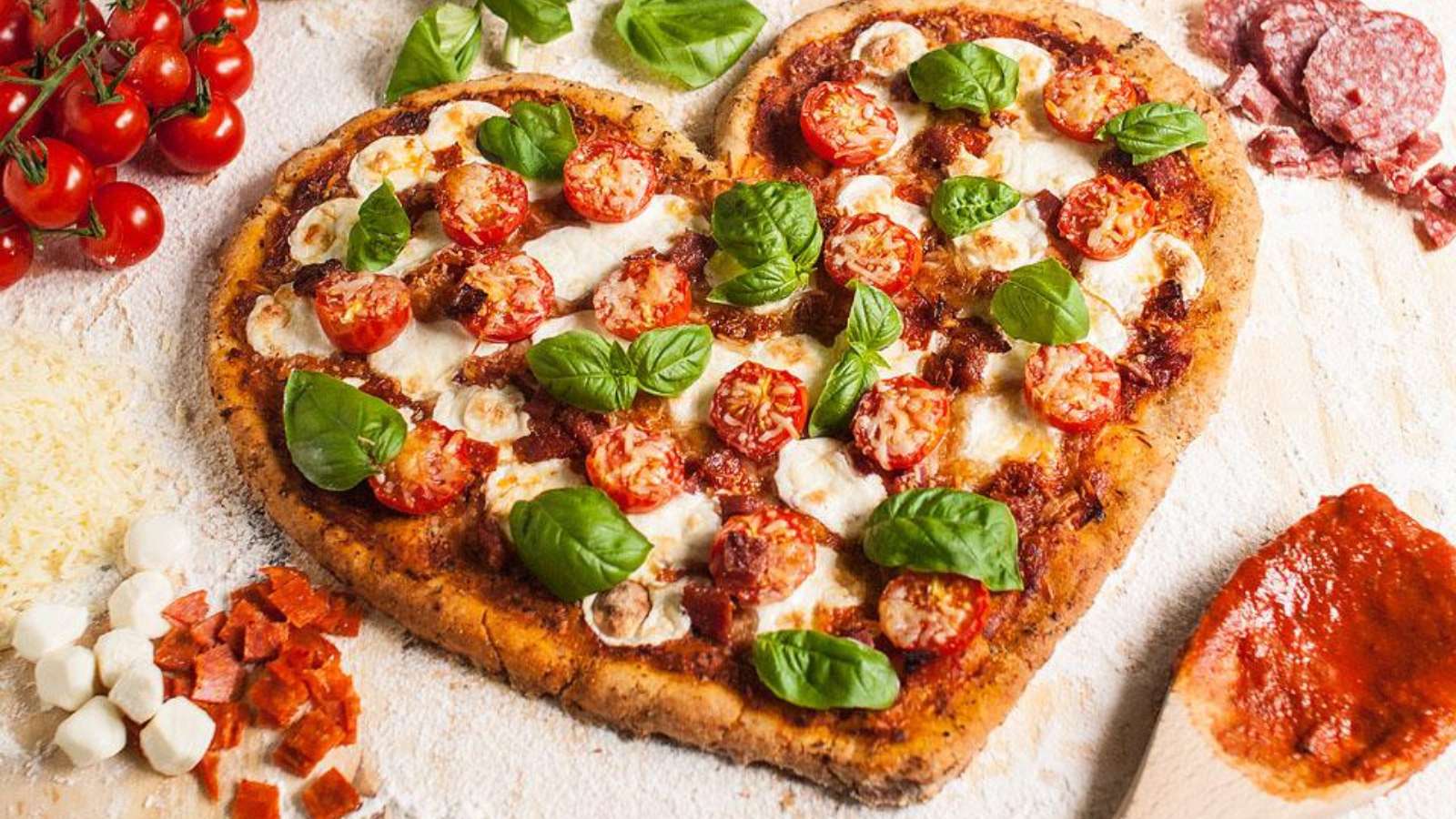 A heart shaped pizza with tomatoes, basil and other ingredients.