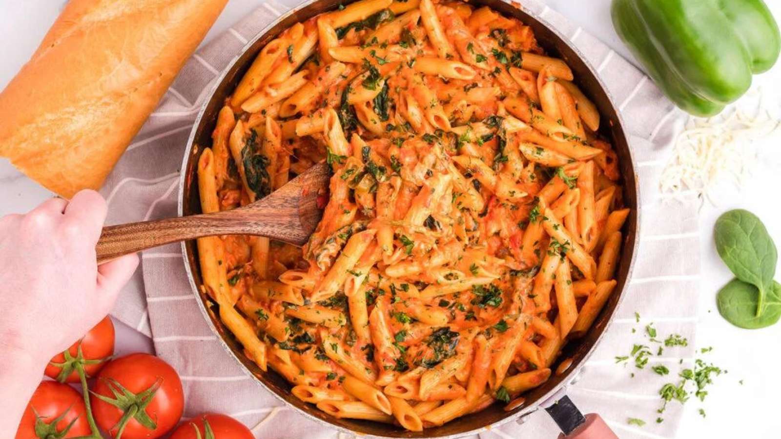 Penne pasta with spinach and tomatoes in a pan with a wooden spoon.