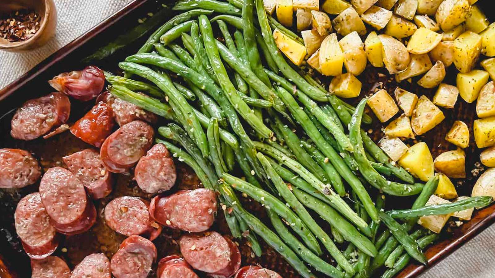 Sausage, green beans and potatoes on a baking sheet.
