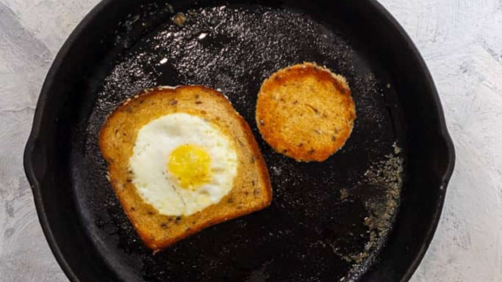 A fried egg on toast in a skillet.