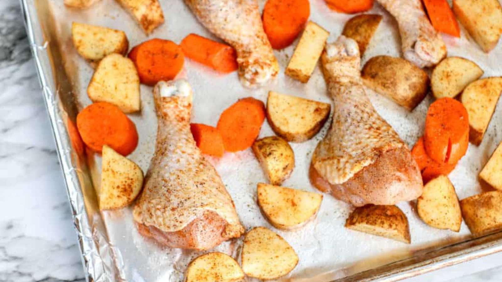 Roasted chicken with carrots and potatoes on a baking sheet.