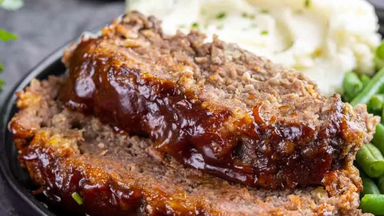 Meatloaf on a plate with green beans and mashed potatoes.
