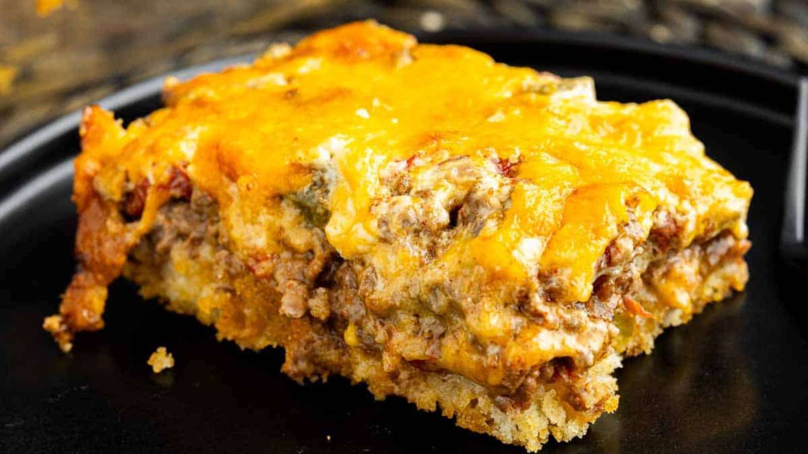 A piece of meat and cheese casserole on a black plate.