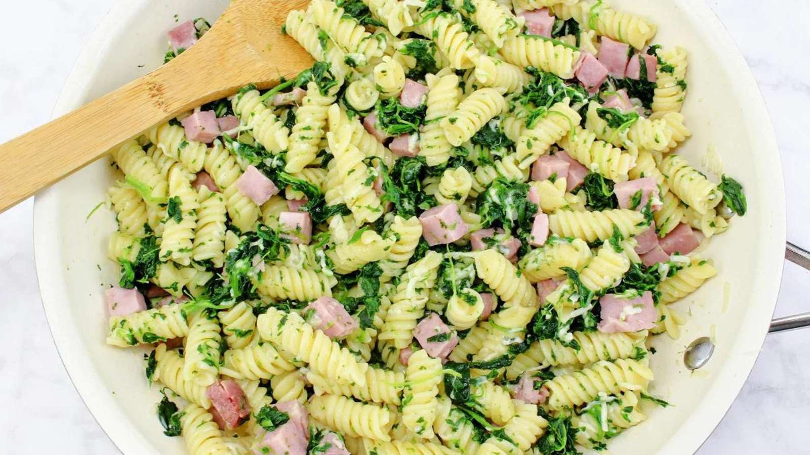 A bowl of pasta with ham and spinach.