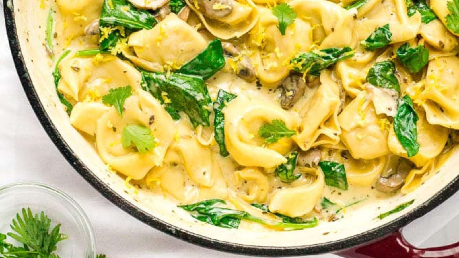 A bowl of pasta with spinach and mushrooms.