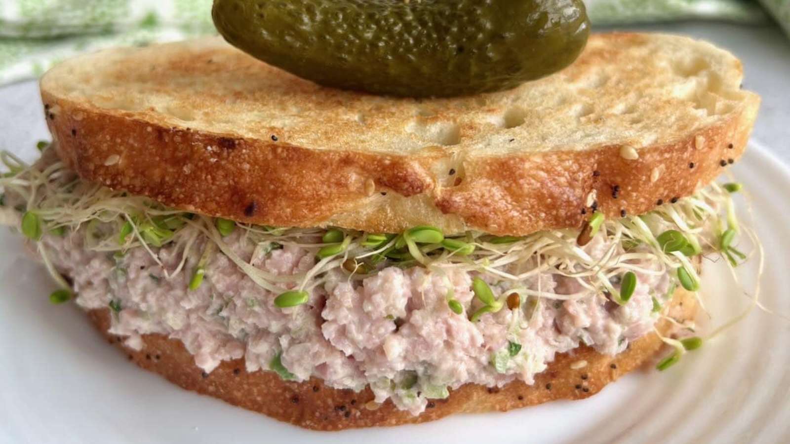 A sandwich with ham salad and sprouts on a plate.