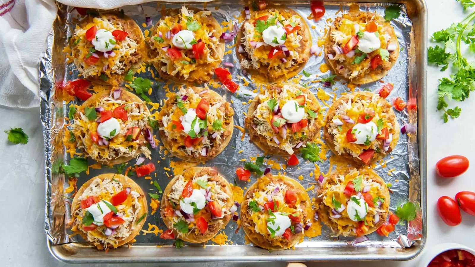 Tostadas on a baking sheet with tomatoes and sour cream.
